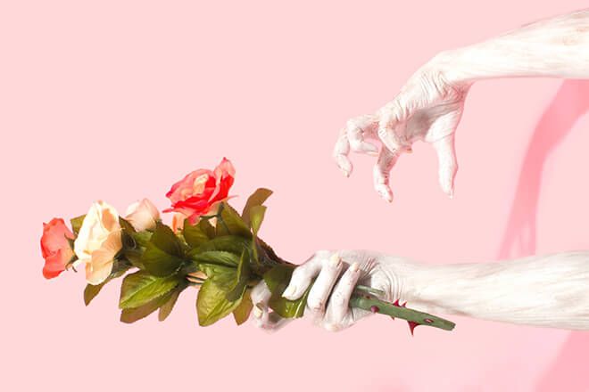 en hånd som holder blomster og en annen hånd som angriper den hånden med rosa bakgrunn