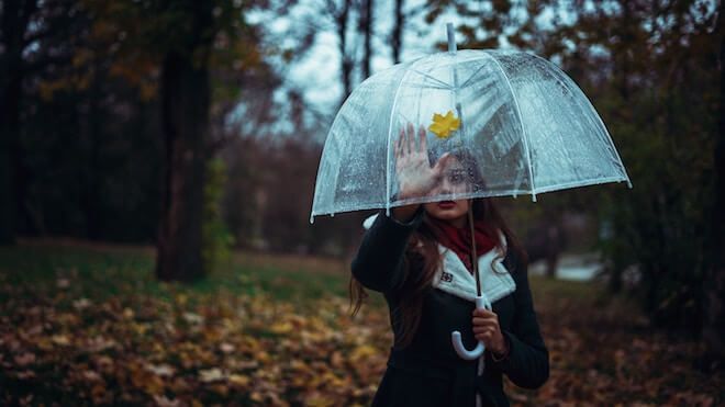 Жена с прозрачен чадър посяга към жълт лист