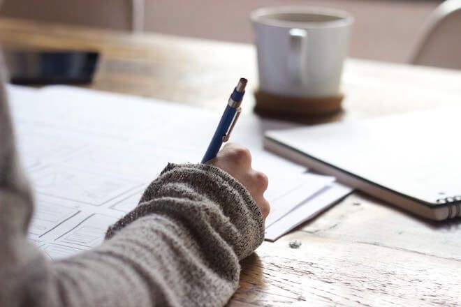 Una mujer escribiendo en un cuaderno con un suéter grueso y un poco de café