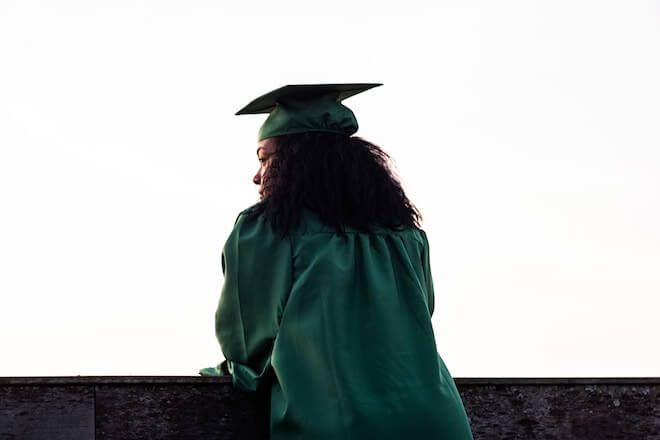 Žena stoji iznad balkona s diplomskom kapom i odjevenom u haljinu
