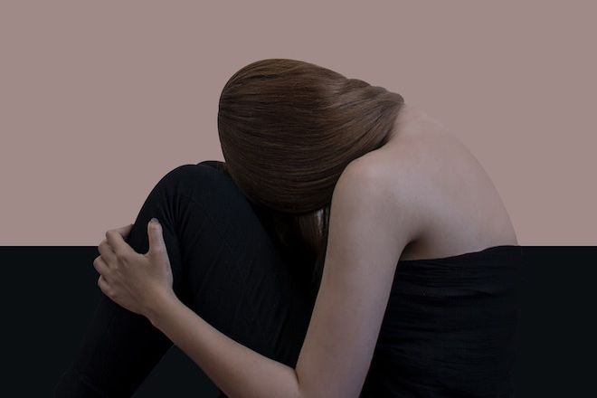 En kvinne med hodet på knærne dekket av et sort ark