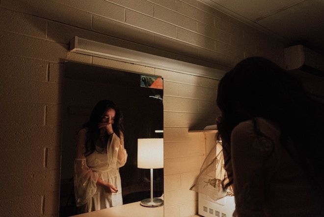 En kvinne gråter mens hun ser inn i speilet.