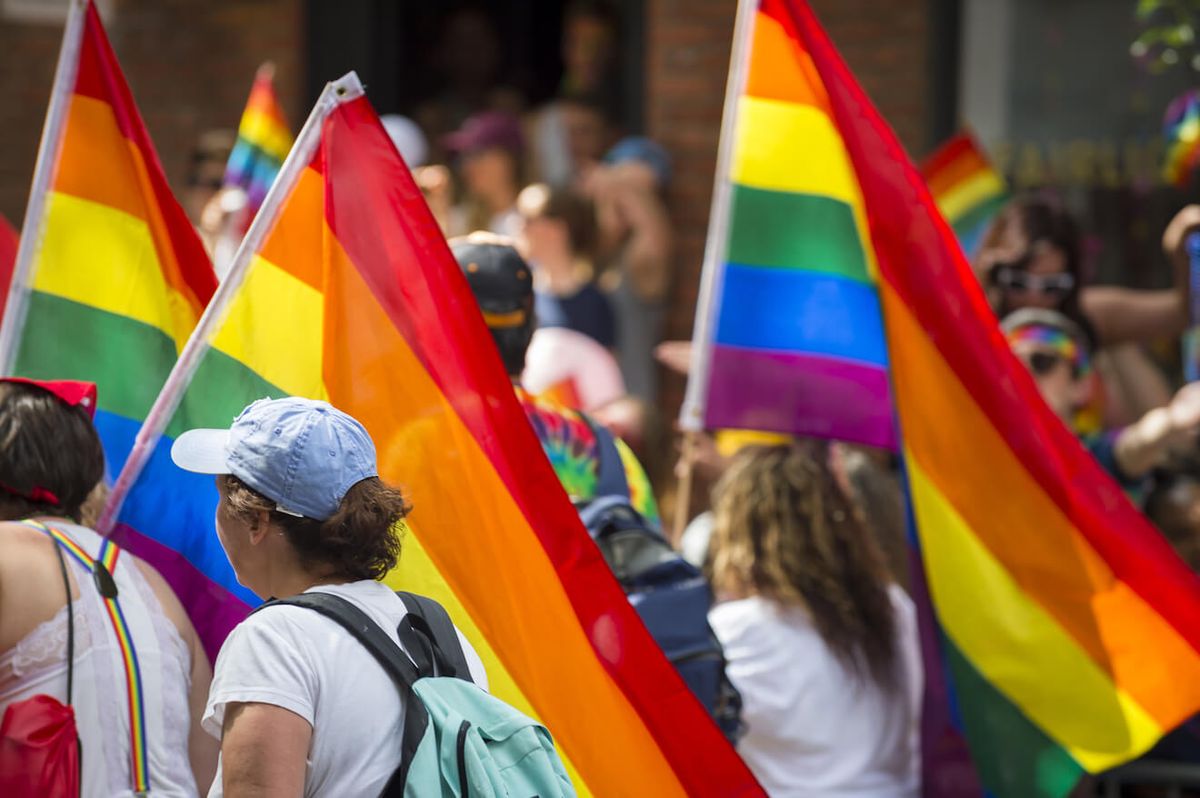 Folk marcherer i gay pride-parade med regnbueflag