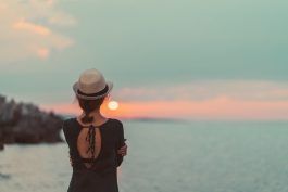 Vista trasera de la mujer con sombrero para el sol mirando la puesta de sol sobre el agua
