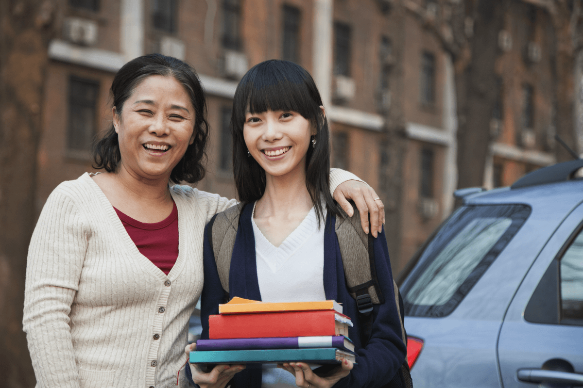 Hija de mamá asiática sosteniendo libros universitarios cerca del coche