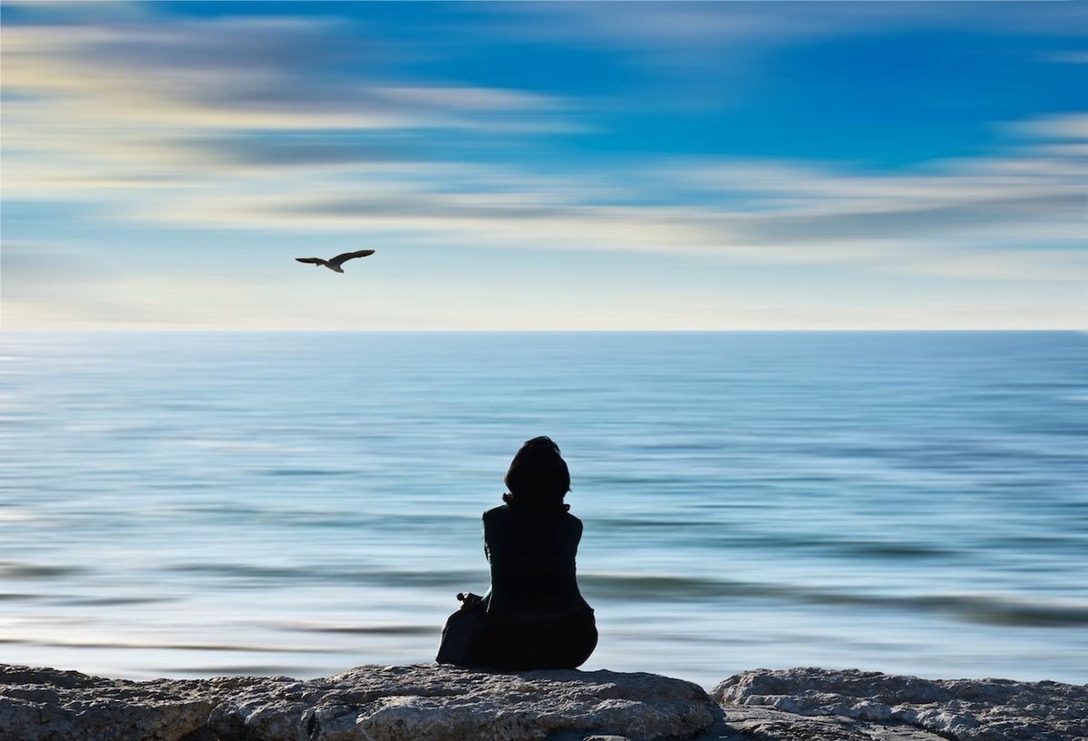 nő ül a sziklák, az óceán, egy madár a távolban