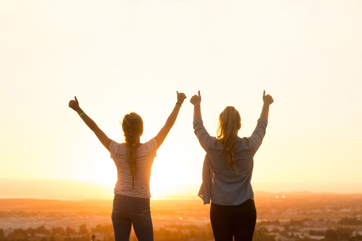 To kvinder med armene op foran solnedgangen