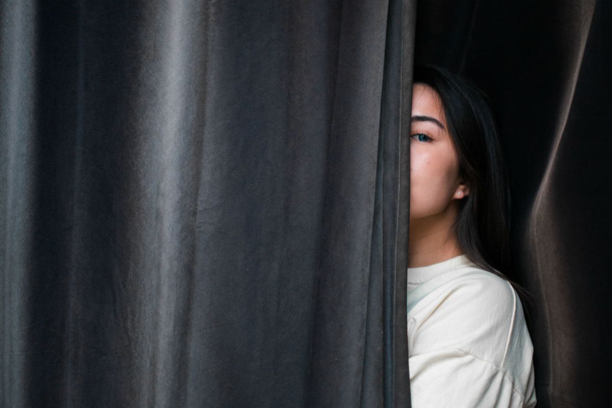 Mujer mirando desde detrás de la cortina gris