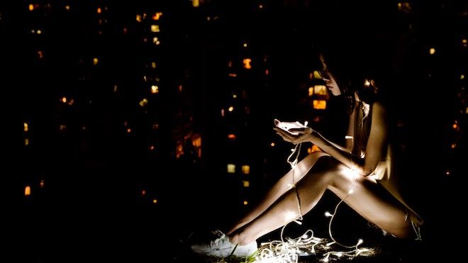 Una adolescente se sienta en la oscuridad en su teléfono