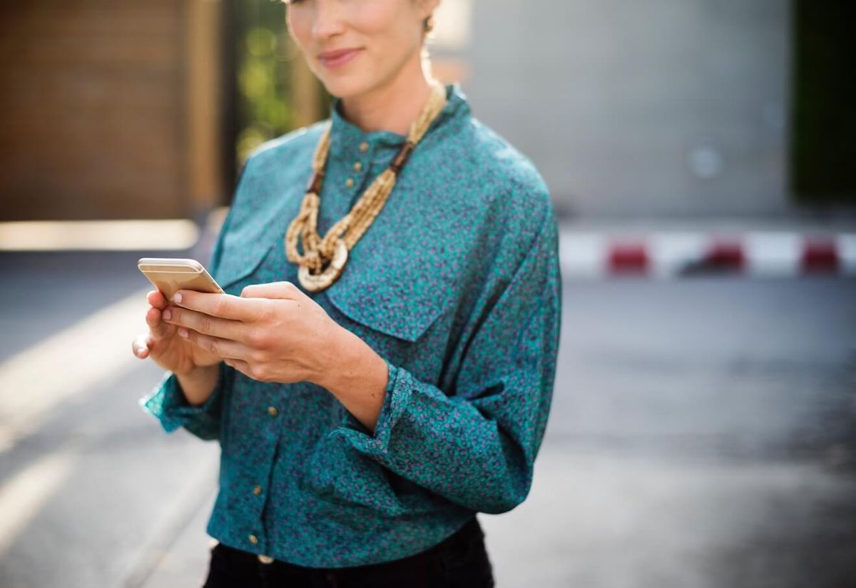 Γυναίκα στο πουκάμισο κιρκίρι που χαμογελά χρησιμοποιώντας το τηλέφωνό της