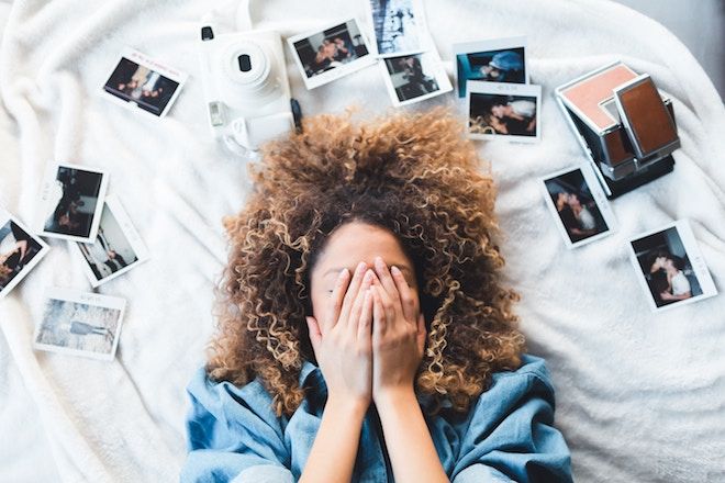 Žena leží na posteli obklopená fotografiami a zakrýva si tvár