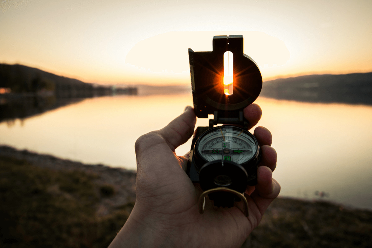 kompass, kas vērsts pret ezeru saulrietā